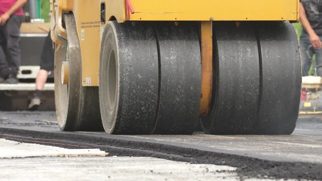 The skating rink is compacting fresh asphalt. Thrombo a new layer of asphalt using a heavy roller. The heavy roller rolls over fresh asphalt several times to achieve the required density
