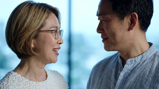 Happy Asian Middle-Aged Couple Sharing a Warm Conversation Indoors Near Window