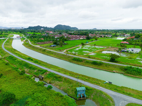 Aerial drone view of a waterway canal by green paddy fields at Bintong, Perlis, Malaysia