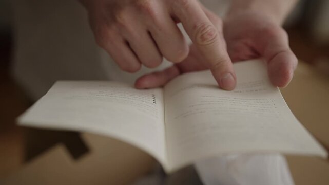 Ufa, Russia - 17 May 2026. Male hands holding small open book, with finger pointing to text, reading instruction manual and flipping through pages to find important information, slow motion