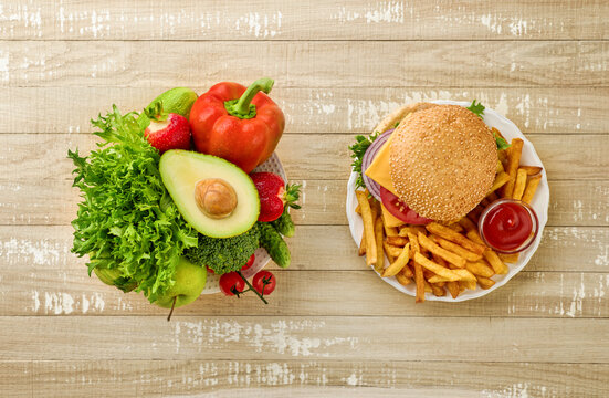 Flat lay of healthy vegetables with avocado, lettuce, broccoli and bell pepper next to burger, fries and ketchup, visual comparison of balanced nutrition and unhealthy fast food choices.