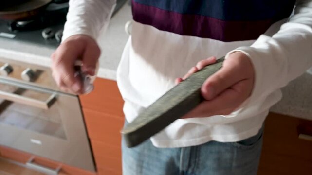 Close-up of a man sharpening a stainless steel kitchen knife with a traditional whetstone at home