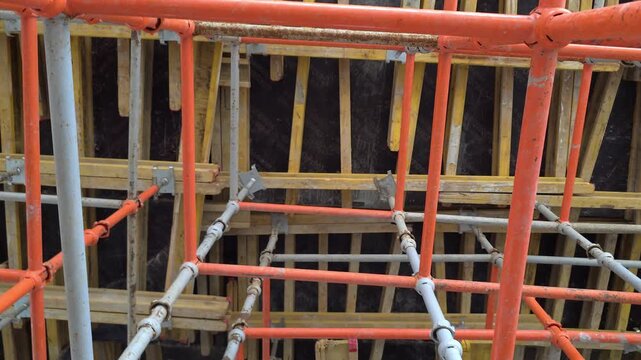 Moscow, May 20 2026, Close-up view of orange and gray metal scaffolding. Rust spots appear on vertical structural beams. Interlocking pipes create a secure grid. Industrial construction environment in