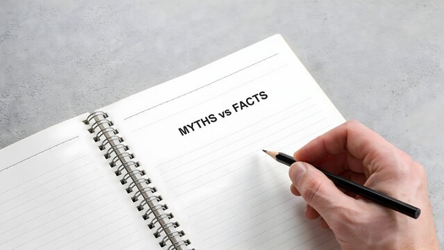 Hand holding a pen to write myths vs facts in a spiral notebook with fact checking notebook falsehood information analysis clarification comparison decision reasoning research education