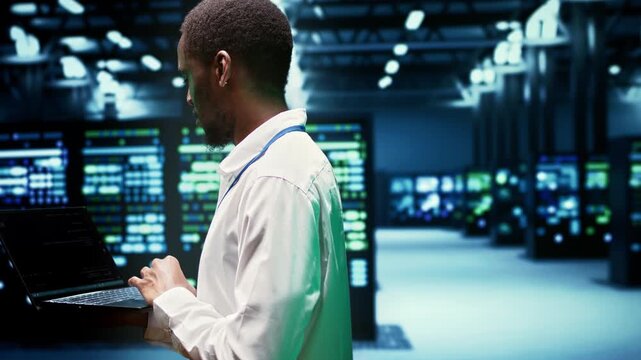African American engineer walks among supercomputers in a data center, overseeing computing resources, data storage equipment and network operations around data center supercomputers.