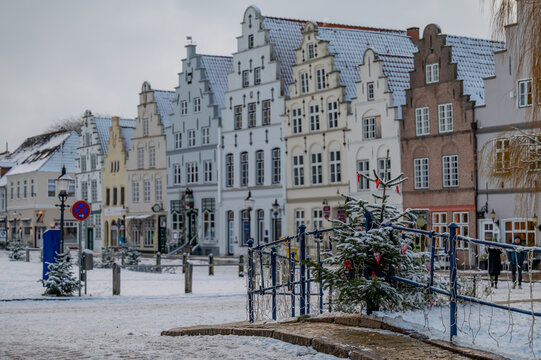 Historic market square in Friedrichstadt, Germany with traditional Dutch-style step-gabled houses lined up under  fresh layer of snow and decorated Christmas tree in the foreground.