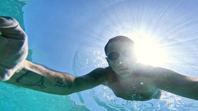Slow-motion of a man swimming underwater in the Mediterranean Sea. The man is of Caucasian origin, is forty-two years old, has short hair and has swimming glasses on his face