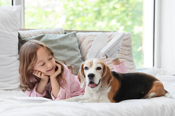 Obraz premium Cute little girl with Beagle dog reading book on bed in bedroom