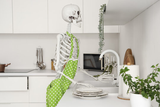 Human skeleton model with apron washing dishes in kitchen