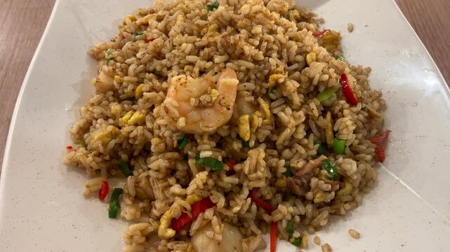 Close up top view of a plate of delicious homemade Indonesian nasi goreng, egg fried rice topped with fried shallots and served with prawns on a white plate. Popular Asian comfort food and street food