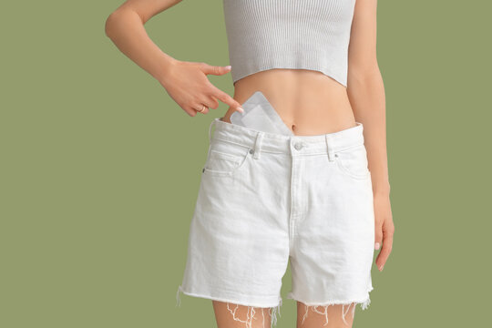 Young woman pointing at applied medical patch after appendectomy surgery on green background