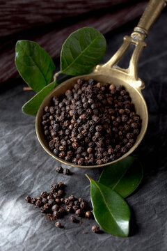 Black peppercorns in a brass trowel with leaves