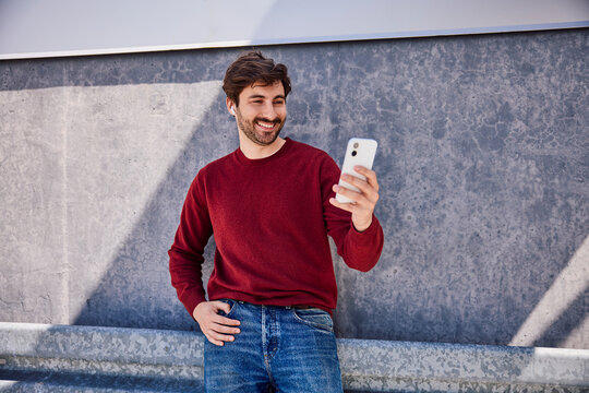 Smiling user looking at smartphone with earbuds outdoors
