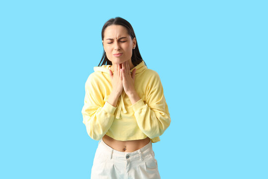 Young woman suffering from sore throat on blue background