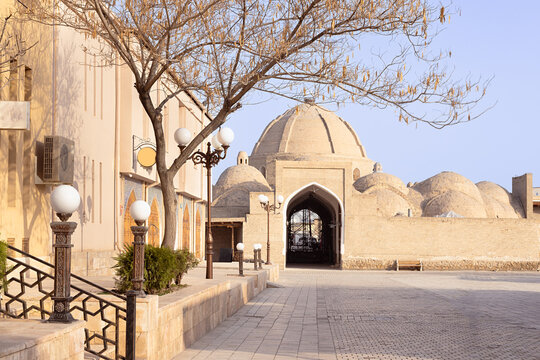 Toqi Zargaron trading dome entrance in Bukhara with arched gateway and brick domes on an empty sunlit street. Ideal for travel publications, heritage brochures, and Central Asian tourism materials.