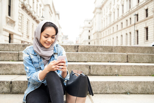 UK, England, London, young woman wearing hijab using cell phone in the city