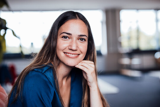 Happy young businesswoman with hand on chin in office