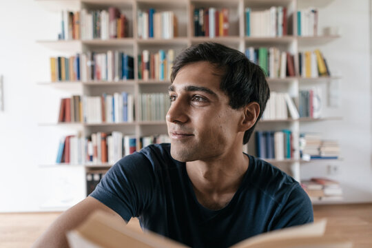 Smiling young man with book at home looking sideways