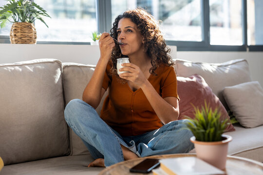 Young woman eating yogurt on sofa at home