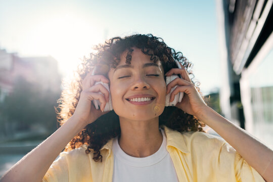 Smiling woman listens to music on headphones outdoors in the city
