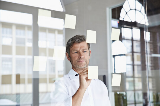 Businessman writing on sticky note on glass pane in office