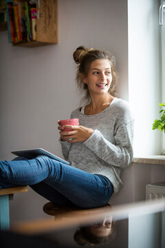 Smiling woman sitting on stool with cup and tablet