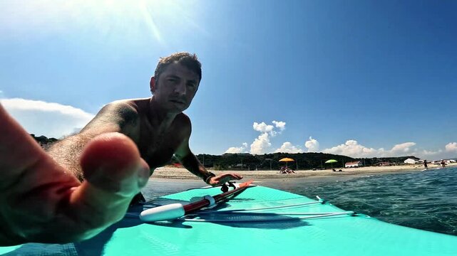 Slow-motion of a man who turns on an action cam placed on a stand-up paddle board and prepares to begin a tour of the Mediterranean Sea