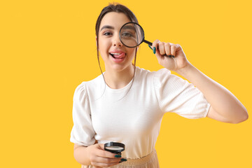 Young woman with magnifiers on yellow background