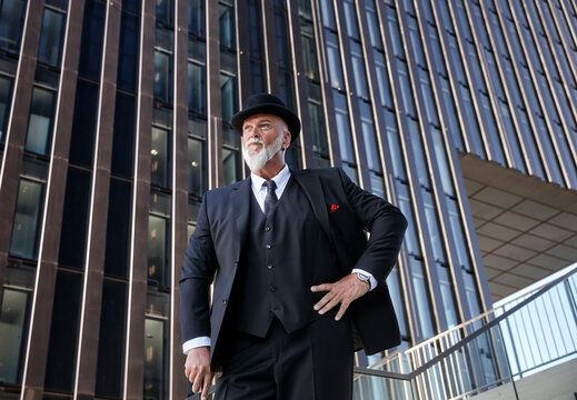 Elegant businessman with bowler hat and walking cane, standing on stairs in the city