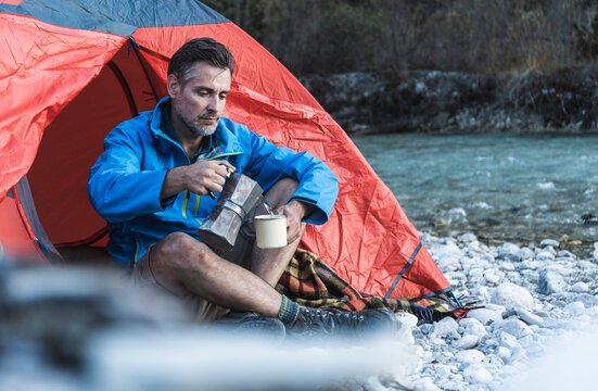 Mature man camping at riverside, espresso maker and cup