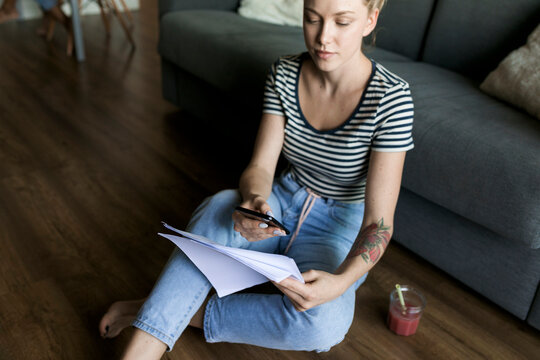 Young woman sitting on floor with cell phone and papers