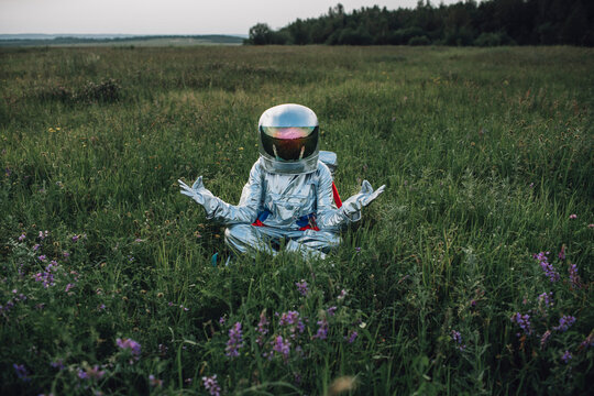 Spaceman exploring nature, sitting in meadow, meditating