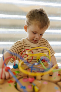 Cute little boy playing with wooden bead maze toy in playroom