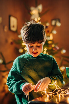 Boy holds glowing fairy light near Christmas tree at home