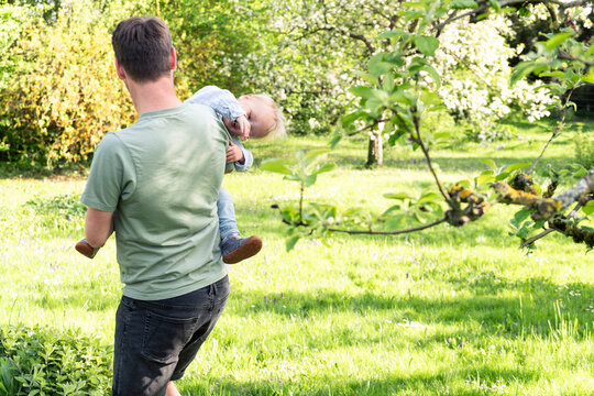 A father carries his baby son while playing in a green spring garden