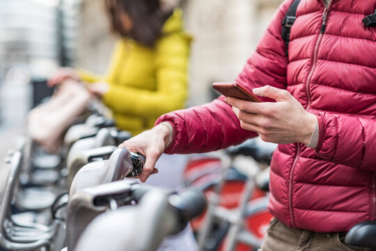 UK, London, young man renting bicycle from bike share stand in city, close-up