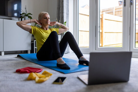 Determined woman doing crunches while e-learning through online tutorial at home