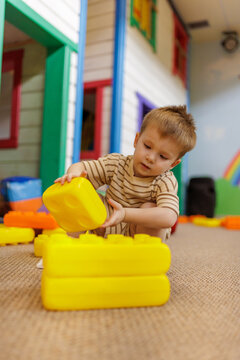 Focused toddler child stacking big construction bricks at kids club