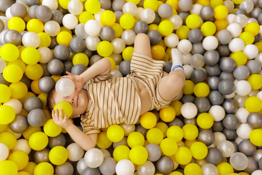 Cute little boy hiding his eyes with plastic balls in ball pit