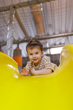 Happy little boy smiling and lying on top of yellow plastic slide