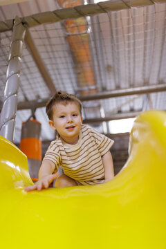 Happy little boy smiling and sliding down a yellow plastic slide