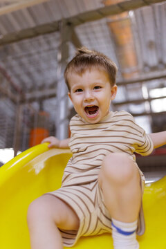 Excited little boy shouting with joy while sliding down a yellow slide