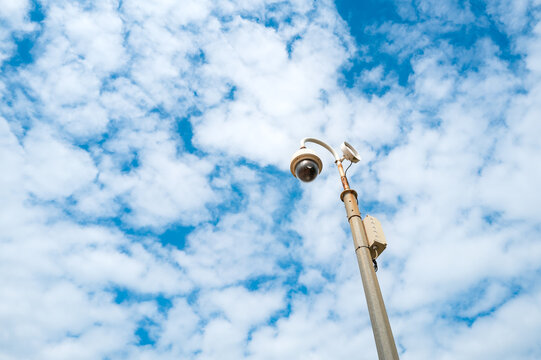 Vertical view of a seaside remote CCTV dome camera seen against a summer sky. The salt air has called rust of the lamppost. In an area for low level crime and anti social behaviour.
