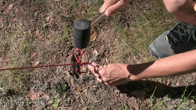 A close up high angle shot of a person hammering a tent stake into the ground