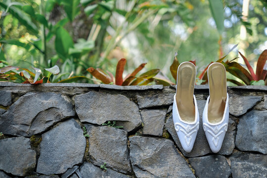 White Bridal Mules on Stone Wall With Tropical Garden Background &mdash; Elegant Wedding Shoes