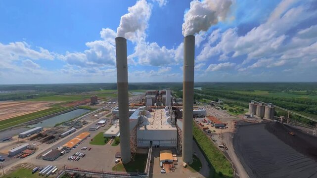 Ascending aerial shot of 2 smokestacks in the foreground, revealing the fossil plant located below