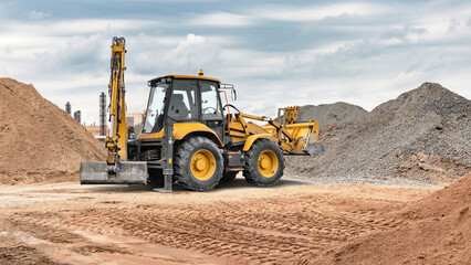 Fototapeta premium Excavator loader is operating at a construction site surrounded by piles of sand and gravel while preparing the ground for a project on a clear day