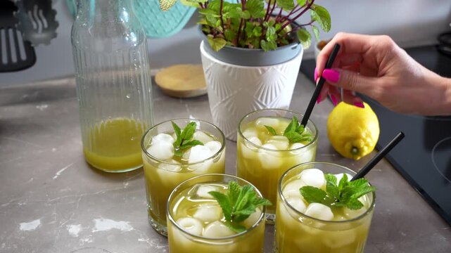 Lemonade is finished with mint, ice cubes and black straws on a kitchen counter, static close-up shot.