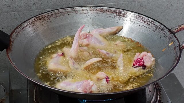 Chicken wings frying in bubbling hot oil in a pan. Close-up of crispy poultry cooking at home, highlighting deep frying, homemade food, and kitchen preparation.