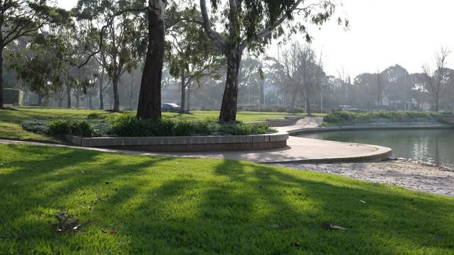 A scenic public parkland and lakeside reserve features a lush green grass lawn within the master-planned estate of Sanctuary Lakes, traffic in background. Suburb of Point Cook, Melbourne, Australia. 